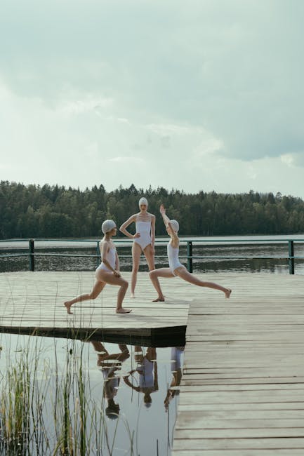 Woman performing a yoga pose on a wooden pier next to a serene lake at sunrise